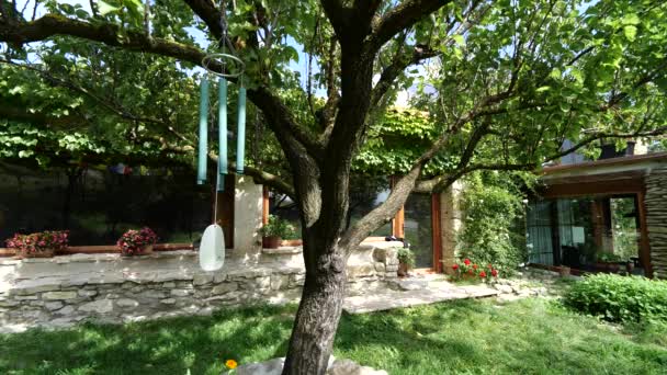 Вітер дзвоник висить на дереві в красивому саду будинку — стокове відео
