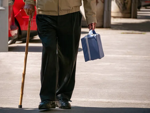 Yaşlı adam küçük bir bavul ve sopayla yürür