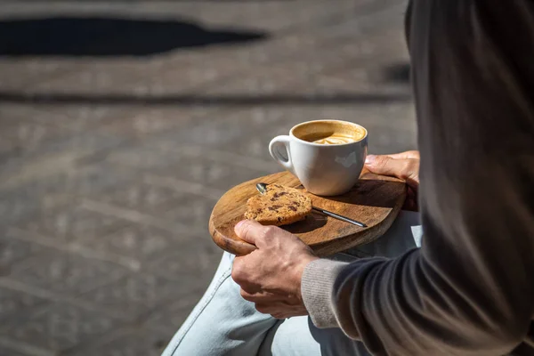 Hombre sentado en la cafetería de la calle con café y galletas en bandeja de madera —  Fotos de Stock