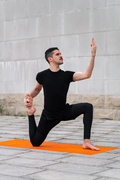 Snygg sportig latin man utövar i en stad, gör yoga, fitness eller pilates träning, sitter i variation av enbent kung duva Pose. — Stockfoto