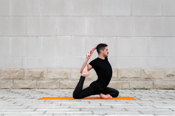 Fešák sportovní latinsky muž cvičení ve městě, dělá jógu, fitness nebo pilates trénink, sedí v One Legged King Pigeon Pose. — Stock fotografie