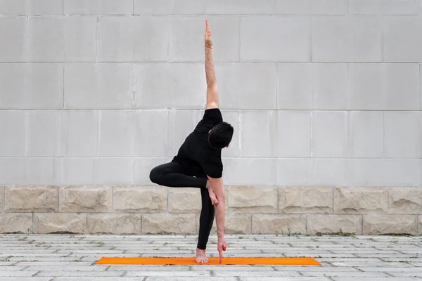 Ung man i svart sport kläder utför balans och stretch motion inspirerad av yoga, utomhus. — Stockfoto