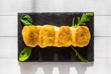 Sarı soslu kroketler, mısır salatası ve siyah taş tabakta roka. Beyaz arkaplanda üst görünüm