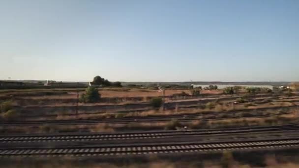 Uitzicht op een landschap vanuit het raam van de rijdende trein bij zonsondergang. Industriegebied met magazijngebouwen — Stockvideo