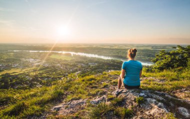 Bir kız uçurumun ve gün batımı ve nehir Vadisi bakarak kenarına oturur