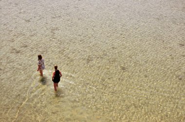 Sidari, Korfu Adası, Yunanistan; Haziran 2019. İki genç kadın sıcak bir günde ferahlatıcı bir şeyler bulmak için denizde yürür..
