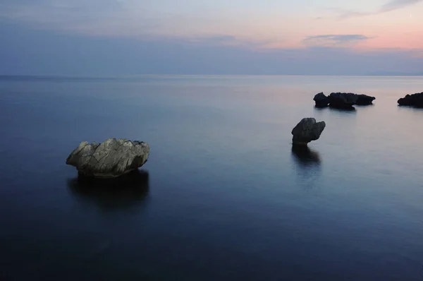 Twilight at sea. Rocks, calm sea and the last reflection of the sun.