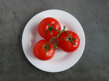 Beyaz tabaktaki taze domatesler ve çimento arka planı. Yukarıdan bak. su damlaları.