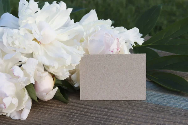 Mock up, greeting card. white flowers of peonies and a card card on a wooden background. postcard