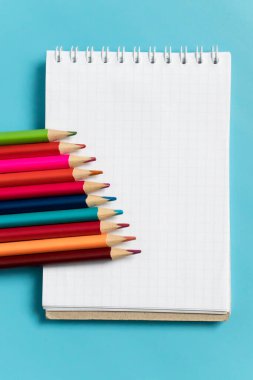 Mavi arka planda renkli kalemler ve defter. Mesajlaşma yeri, okula dönüş. maket, dikey