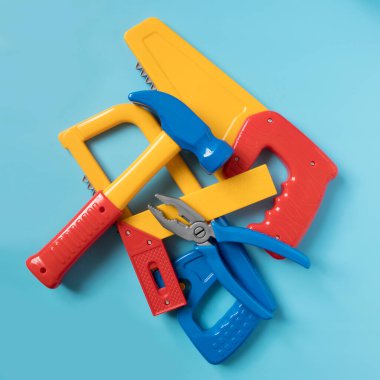 Mavi arka plandaki bir yığın plastik oyuncağın içinde. Çekiç, testere, müfreze, cetvel