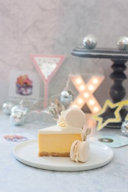 Bir parça mango portakallı cheesecake üzerinde beyaz makarna ile süslenmiş, gri zemin üzerinde X-harfi, yıldızlar, yıldız gözlükleri ve kağıt bardak şarap var. 