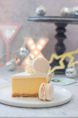Bir parça mango portakallı cheesecake üzerinde beyaz makarna ile süslenmiş, gri zemin üzerinde X-harfi, yıldızlar, yıldız gözlükleri ve kağıt bardak şarap var. 