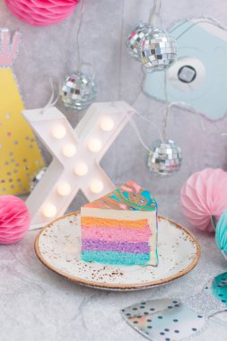 Gri arkaplanda gökkuşağı peynirli kek, X harfli, kağıt topaklı ve çelenkli.