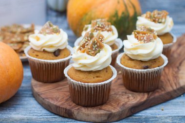 Krem peynirli krema, akçaağaç şurubu, ceviz ve ahşap arka planda karamel ısırıkları ile süslenmiş balkabağı kekleri..