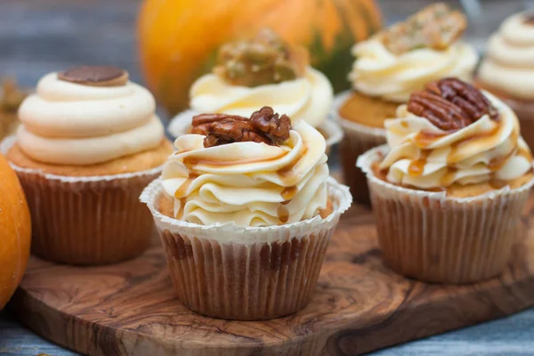 Krem peynirli krema, akçaağaç şurubu, ceviz ve ahşap arka planda karamel ısırıkları ile süslenmiş balkabağı kekleri..