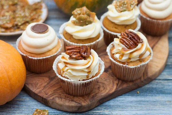 Pumpkin cupcakes decorated with cream cheese frosting, maple syrop, pecan nuts and caramel bites on rustic wooden background.