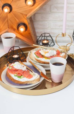 Krem peynirli tost, somon, avokado ve iki fincan kahve ile haşlanmış yumurta. Arka planda yanan mumlar ve retro lambaları olan ahşap yıldız..