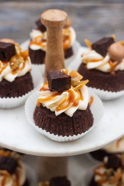 Krem peynirli çikolatalı kekler, tuzlu karamel sosu, çikolatalı kekler ve şekerlemeler. Gri ahşap arka planda mermer pasta.