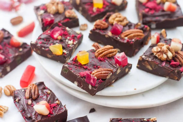 Cevizli çikolata, kurutulmuş ahududu, çilek, çiğnenmiş şeker, lokum ve beyaz tabakta siyah çikolata parçaları..