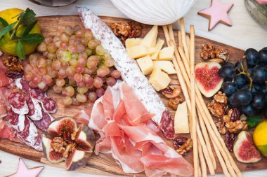 Peynir ve şarküteri servis panosu, parmesan peyniri, jambon, salam, üzüm, incir, ceviz, jambon ve ekmek çubukları. Arka planda güller, balkabakları ve kağıt balonlar var..