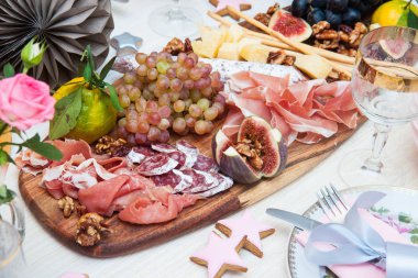 Peynir ve şarküteri servis panosu, parmesan peyniri, jambon, salam, üzüm, incir, ceviz, jambon ve ekmek çubukları. Arka planda güller, balkabakları ve kağıt balonlar var..