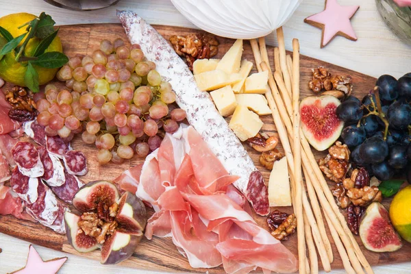 Cheese and charcuterie serving board with parmesan, prosciutto, salami, grapes, figs, bread, pecan nuts, ham and bread sticks. Roses, pumpkin and paper balloons are on the background.