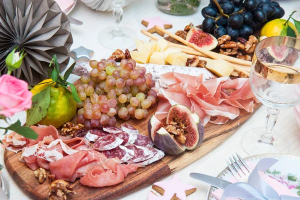 Peynir ve şarküteri servis panosu, parmesan peyniri, jambon, salam, üzüm, incir, ceviz, jambon ve ekmek çubukları. Arka planda güller, balkabakları ve kağıt balonlar var..