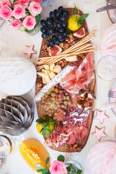 Peynir ve şarküteri servis panosu, parmesan peyniri, jambon, salam, üzüm, incir, ceviz, jambon ve ekmek çubukları. Arka planda güller, balkabakları ve kağıt balonlar var..