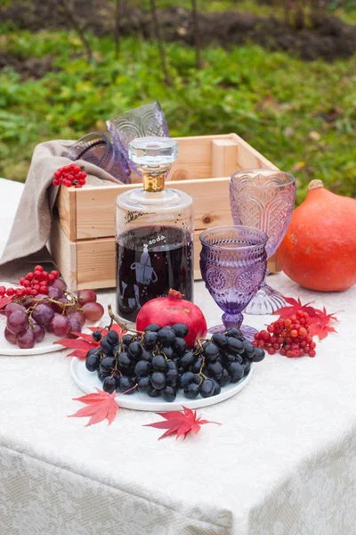 Üzerinde ahşap kutu, şarap bardakları, böğürtlen, üzüm, nar, balkabağı ve kırmızı sonbahar yaprakları olan piknik masası. Açık konum.