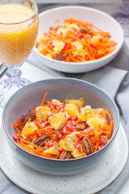 Havuçlu sağlıklı çiğ vejetaryen salatası, nar tohumu, portakal, kabak tohumu, fındıklı fındık. Arka planda bir bardak portakal suyu ve nar..