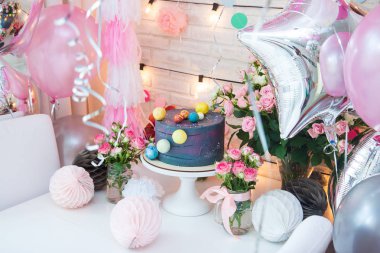 Çikolata toplarıyla süslenmiş doğum günü partisi mavi pastası. Balonlarla, çiçeklerle, gül buketleriyle, sicim lambalarıyla ve kağıt toplarla süslenmiş bir masa.. 