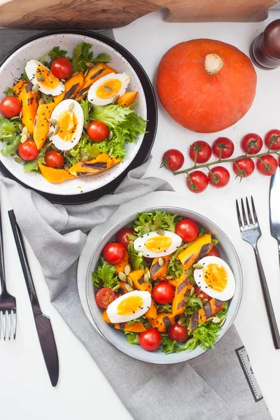 Detox vegetable salad with grilled pumpkin, cherry tomatoes, boiled eggs, seeds and lettuce in grey bowl.