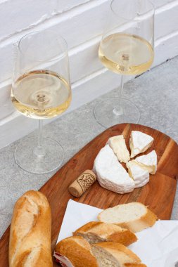 Camembert peyniri, baget ve tahta tahtada iki bardak beyaz şarap. Arkaplan olarak beyaz tuğla duvar.