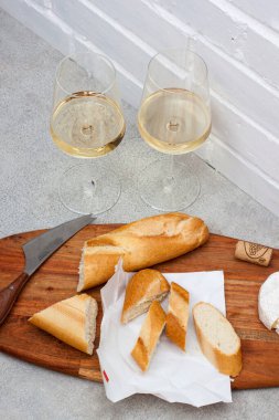 Camembert peyniri, baget ve tahta tahtada iki bardak beyaz şarap. Arkaplan olarak beyaz tuğla duvar.