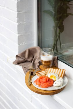 Haşlanmış yumurta, füme somon, kızarmış ekmek ve kahve binanın dışındaki beyaz pencere eşiğinde..