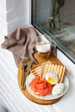 Haşlanmış yumurta, füme somon, kızarmış ekmek ve kahve binanın dışındaki beyaz pencere eşiğinde..