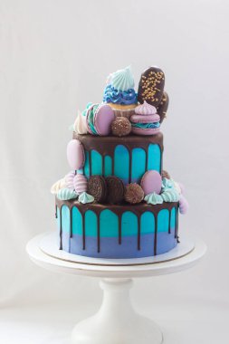 Koyu çikolata, kek, kurabiye, badem kurabiyesi, krema, buzlu şeker ve çikolatayla süslenmiş katlı mavi pasta. Düz gri arkaplan.