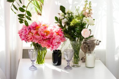 Şakayık buketi ve güller, siyah ve beyaz mumlar, mor şarap bardakları ve pencerenin yanındaki beyaz masada eski çaydanlık..