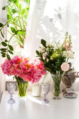 Şakayık buketi ve güller, siyah ve beyaz mumlar, mor şarap bardakları ve pencerenin yanındaki beyaz masada eski çaydanlık..