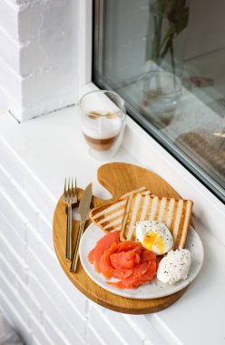 Kahvaltı menüsü: kızarmış ekmek, füme somon, haşlanmış yumurta ve beyaz pencere eşiğinde bir fincan kahve.