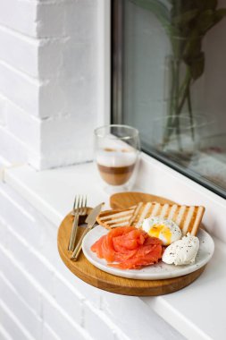 Kahvaltı menüsü: kızarmış ekmek, füme somon, haşlanmış yumurta ve beyaz pencere eşiğinde bir fincan kahve.