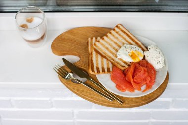 Kahvaltı menüsü: kızarmış ekmek, füme somon, haşlanmış yumurta ve beyaz pencere eşiğinde bir fincan kahve.