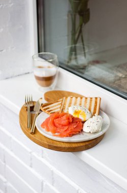 Kahvaltı menüsü: kızarmış ekmek, füme somon, haşlanmış yumurta ve beyaz pencere eşiğinde bir fincan kahve.