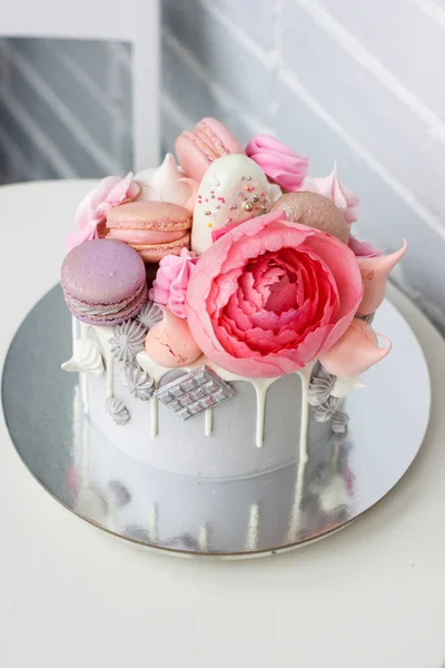 Сучасний сірий торт з рожевими піоновидними квітами, шоколадом і макарунами на весілля або святкування. Білий фон . — стокове фото