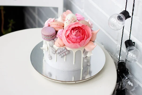 Pastel gris moderno con flores de peonía rosa, chocolate y macarrones para una boda o una celebración. Fondo blanco . —  Fotos de Stock