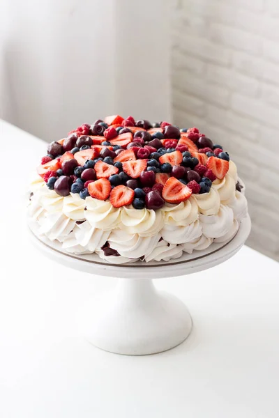 Gâteau meringue à la crème fouettée et baies fraîches, fraises, bleuets, framboises et cerises sur table blanche. — Photo