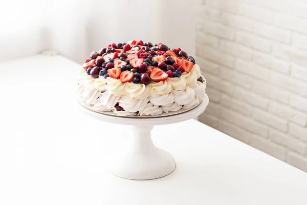 Pastel de merengue con crema batida y bayas frescas, fresas, arándanos, frambuesas y cerezas en mesa blanca . — Foto de Stock