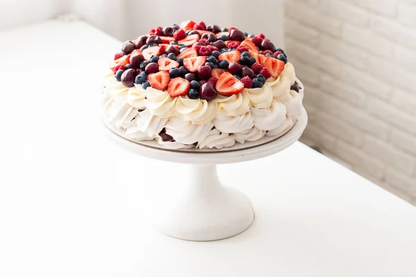 Pastel de merengue con crema batida y bayas frescas, fresas, arándanos, frambuesas y cerezas en mesa blanca . —  Fotos de Stock