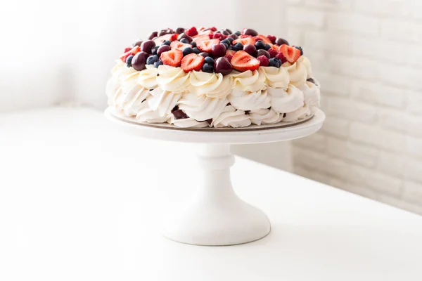 Pastel de merengue con crema batida y bayas frescas, fresas, arándanos, frambuesas y cerezas en mesa blanca . —  Fotos de Stock